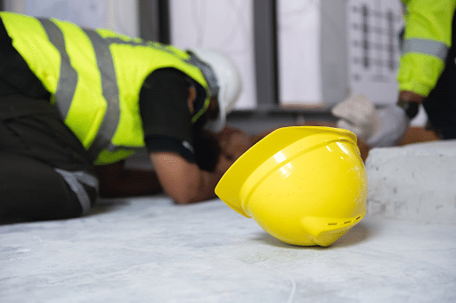 A construction worker injured on the ground after a slip-and-fall accident. His yellow hard hat is next to him.