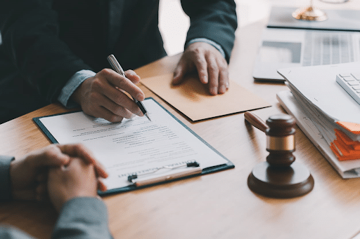 A slip-and-fall accident lawyer filling out paperwork at his desk while he speaks with a client. Next to him is a gavel and an open laptop.