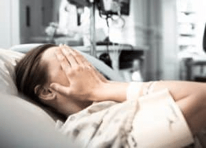 Woman laying in hospital bed with hands over face