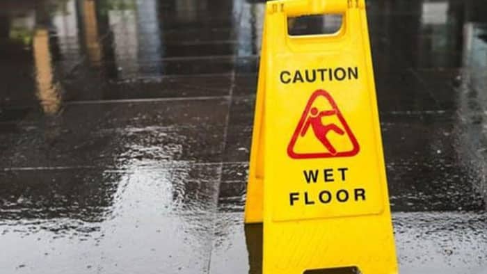A yellow caution: wet floor sign is placed over wet pavement.