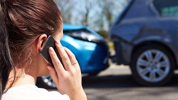 View of a woman on her cell phone calling for help after a car accident. The damaged cars are out of focus in the background.