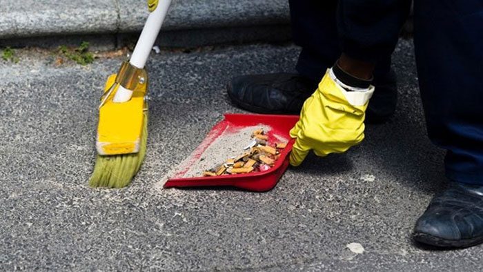 A close-up view of a person sweeping up cigarette butts from the ground.