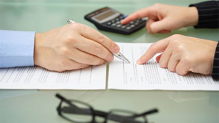 The focus is on the hands of two people calculating an injury bill. Next to them is a pair of glasses and a calculator.