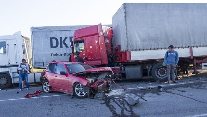 Results from a semi-truck accident. Both the semi-truck and vehicle are badly damaged after a collision. Two people stand near the wreck, looking at the damage.