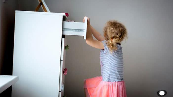A young child is using the top drawer of her dresser to climb up on it, and the dresser is beginning to tilt from the weight.