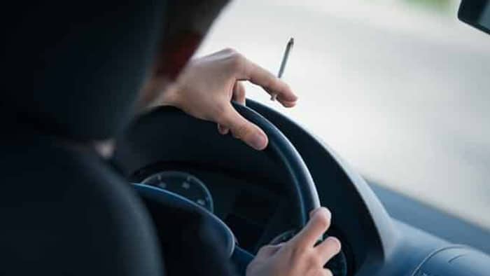 The focus is on someone with their hands on a steering wheel while also holding a joint.