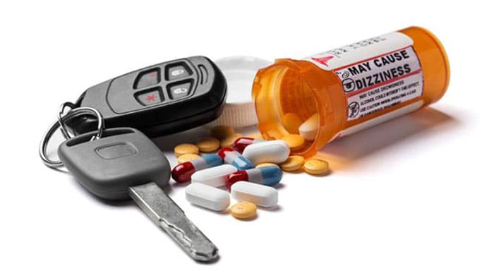 A set of car keys is next to an open and spilled bottle of pills.