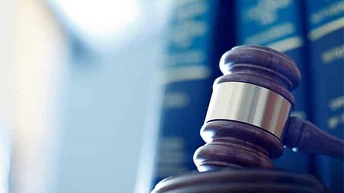 The focus is on a gavel; there are blurred-out books in the background.