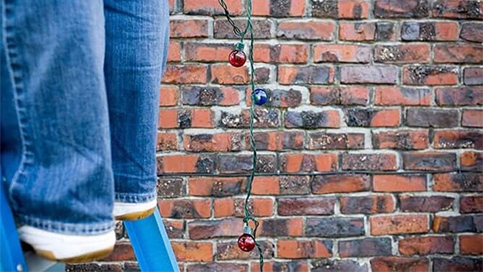 An up-close view of a person's feet as they stand on a ladder. Christmas lights dangle next to them.