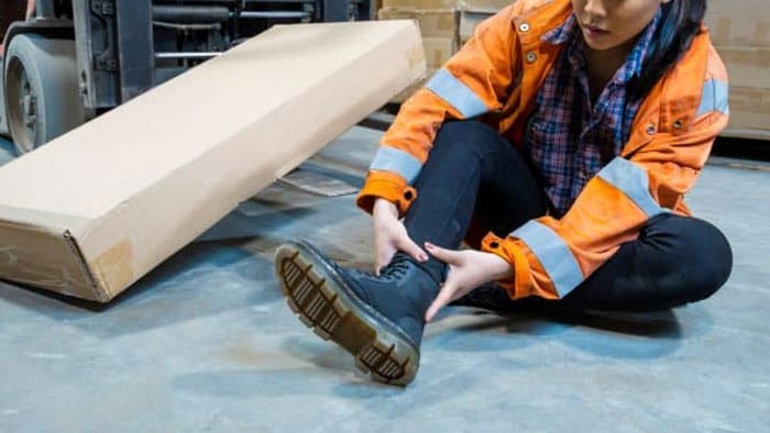 An injured worker clutches her leg after falling near boxes.