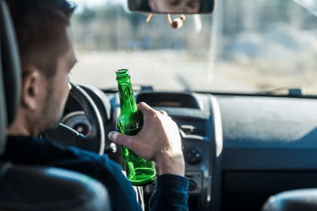 A man sits behind the wheel of a vehicle with a beer in his hand.