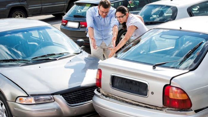 Two people argue in the parking lot, pointing at the damage to their two collided vehicles.