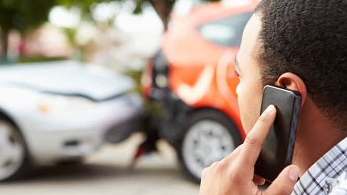 The focus is on a man on his cellphone calling for help after an accident. The cars are out of focus in the background.