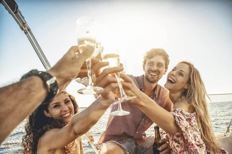 Four friends are toasting their alcoholic drinks together while on a boat.