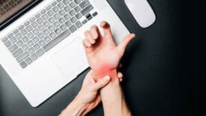 An unidentified person is clutching their wrist in pain near their laptop.