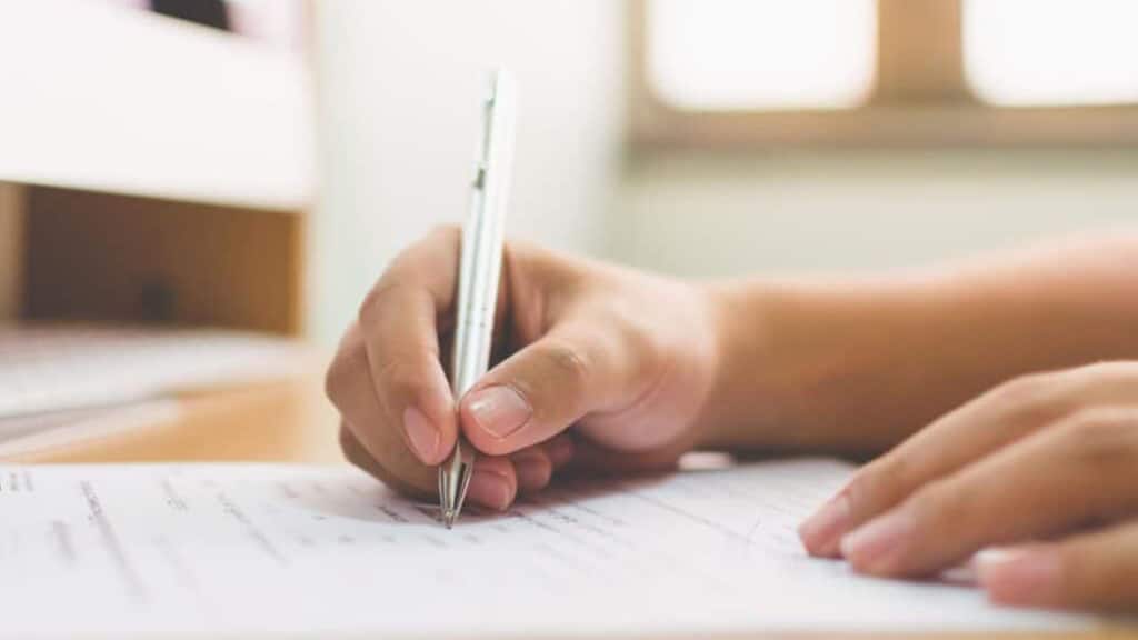 The focus is on a hand holding a pen as a person fills out paperwork.