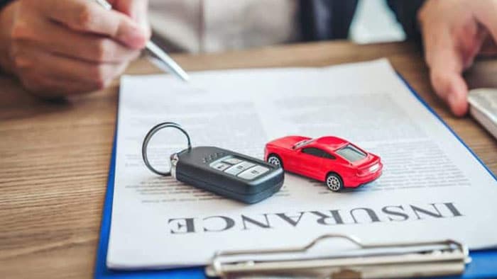 A toy car and a set of car keys are layered on top of insurance documents. The lawyer has a pen, about to sign them/