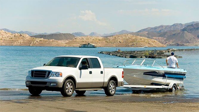 A truck backing a boat into a body of water.