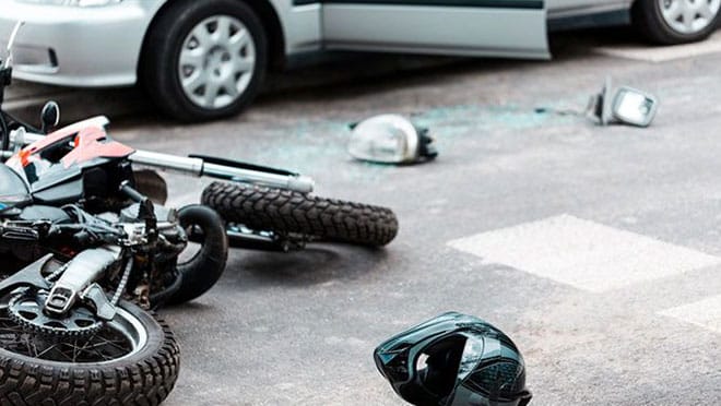 A damaged motorcycle is lying on its side on the ground with a car in the background after an accident.