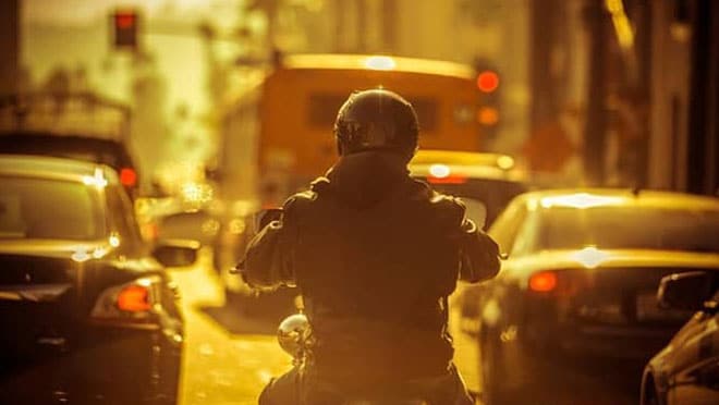 The back of a person riding a motorcycle in traffic.