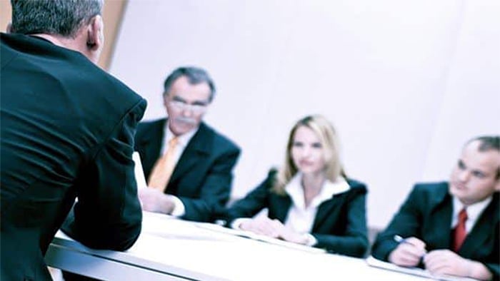 The back of a man addressing three people in front of him at a table.