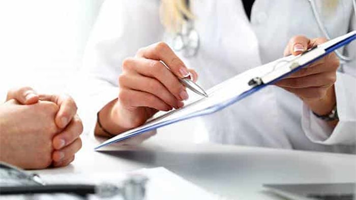 Focus is on a doctor holding a clipboard, showing medical records to their patient.