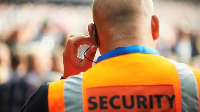 A photo from behind a security guard. His orange vest reads, "Security," and he's pressing his ear piece.