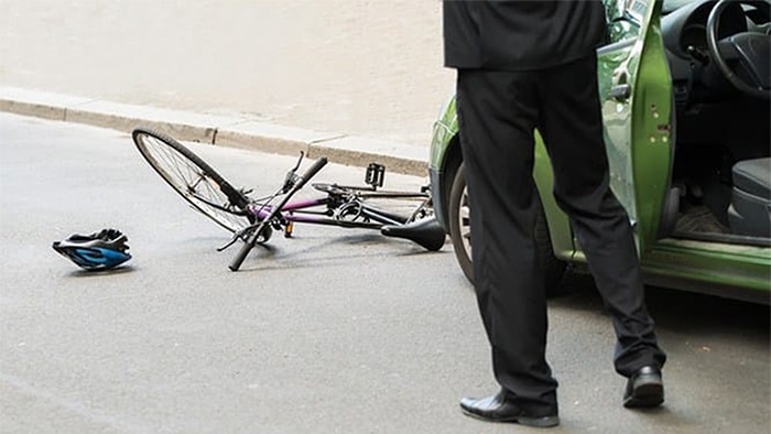 A man stands outside his car as a bicycle lies in front of it in the road after being struck.
