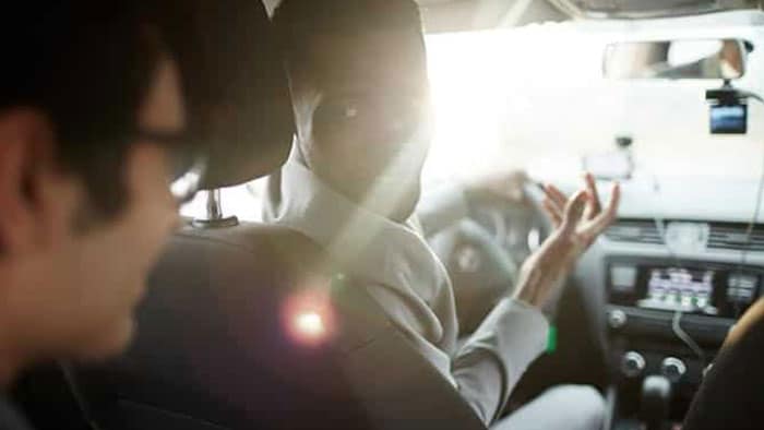 A man in the driver's seat is turned around, talking to his back seat passenger.