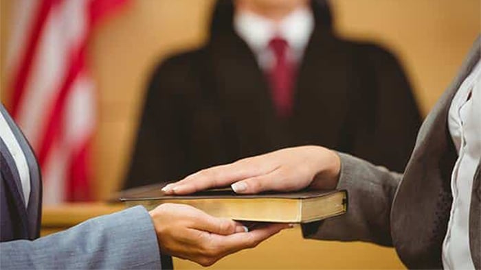 Focus is on a person laying their hand on a book in court, swearing an oath, to tell the truth.