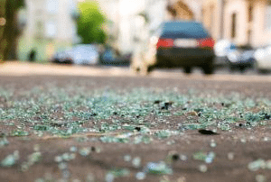 Shattered glass on a roadway, a car is driving away in the distance.