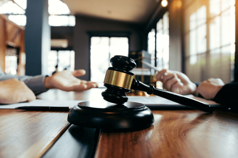 focus is on a gavel. In the background a lawyer speaks with their client.