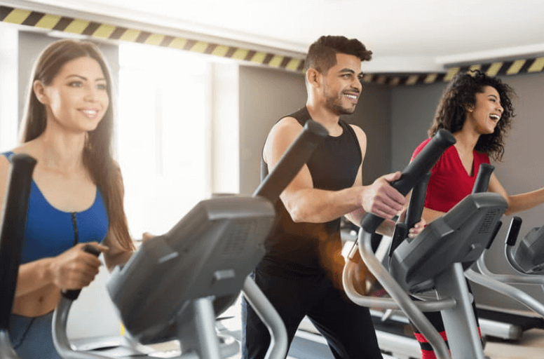 shows three gym-goers in a row on ellipticals 