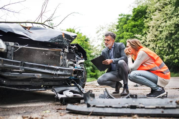 Two people are inspecting the damage on a vehicle after an accident.