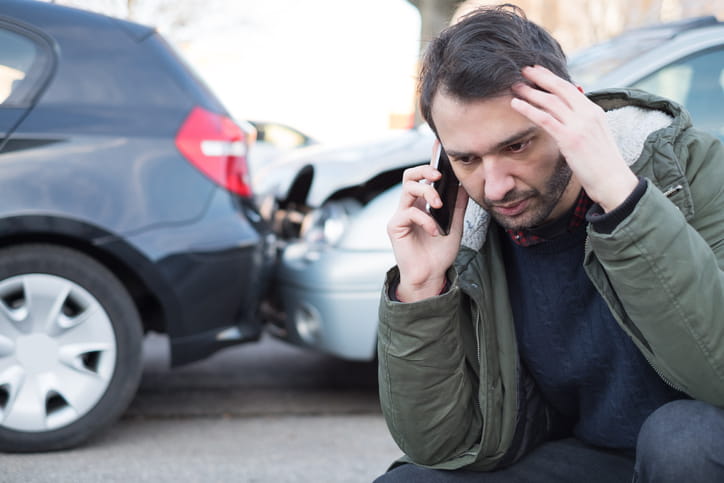 a man on a cellphone, with a car accident pictured in the background.