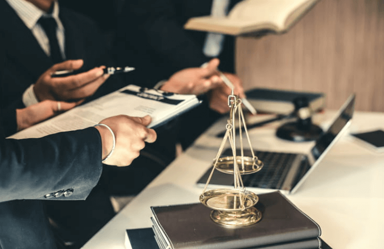 Claim Delays 1 Focus is on a lawyer's hands, holding paperwork to show their client, along with a scales of justice stacked on books on their desk.