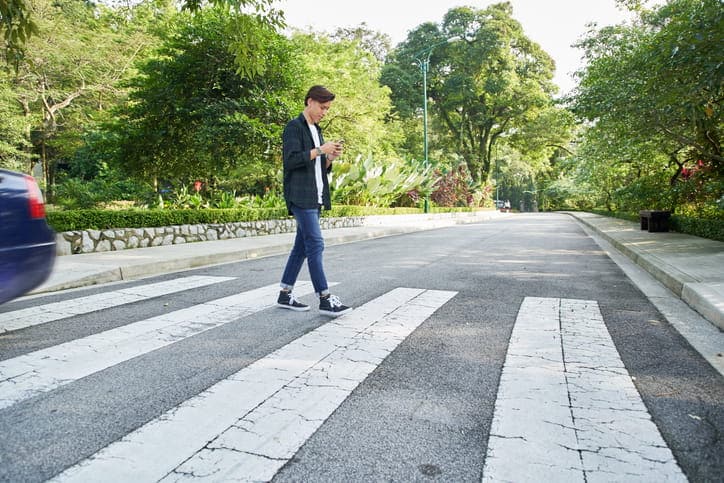 A person walking across a cross walk while looking down at their cellphone.