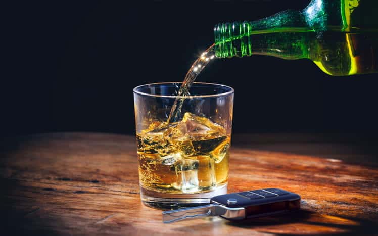 A photo of alcohol being poured into a glass next to a set of car keys.