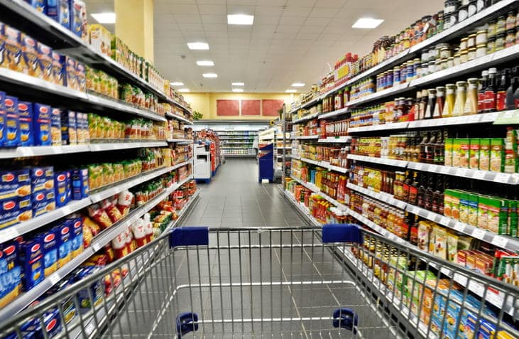 Focus is on a shopping cart within a grocery aisle.