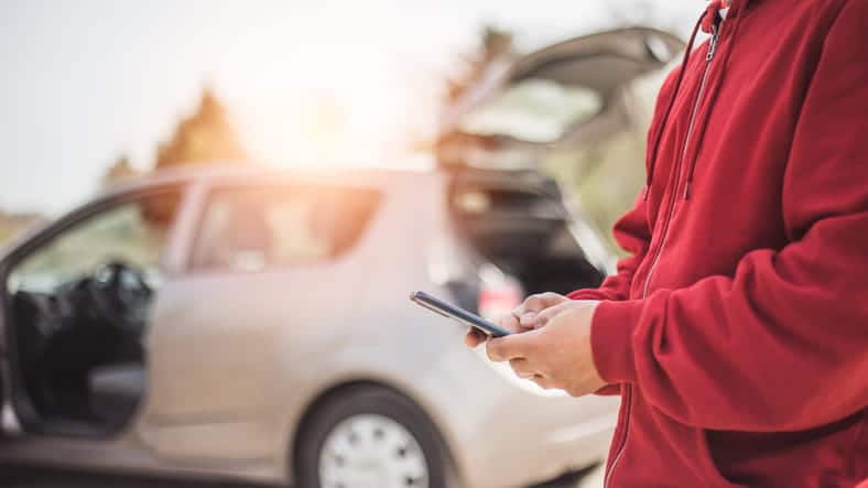 Focus is on an unidentified person dialing their phone for help after a car accident. The car is blurred out in the background.