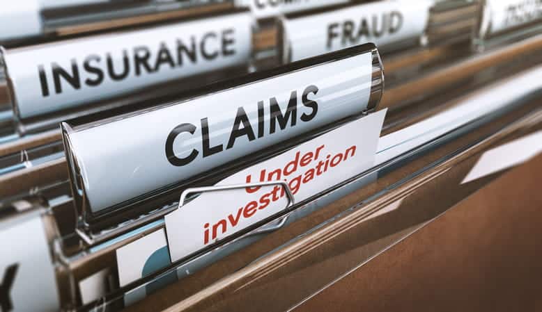 An up-close view of the inside of a filing cabinet with folders labeled "insurance" "fraud" "claims" and "under investigation."