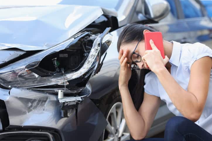 A woman rubbing her forehead while on the phone, upset, after a car accident.