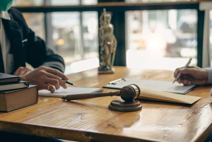 A car accident lawyer discussing the case with their client. On their desk is paperwork, a stack of books, and a gavel.