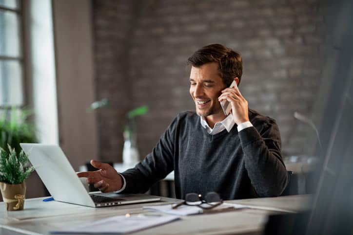 A man is on the phone, communicating with his personal injury lawyer. His laptop is open in front of him, along with paperwork.