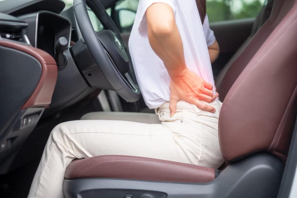 A woman holding her back while sitting in the driver's seat of a car after suffering from a personal injury.