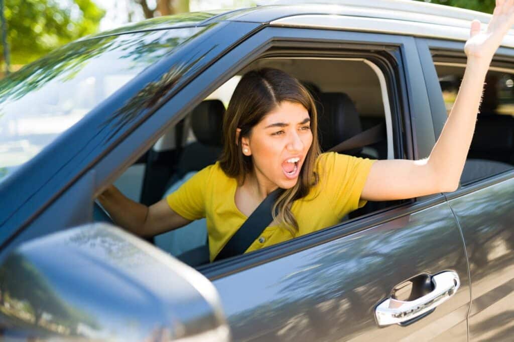 A young woman who is yelling out of her car window as she experiences road rage.
