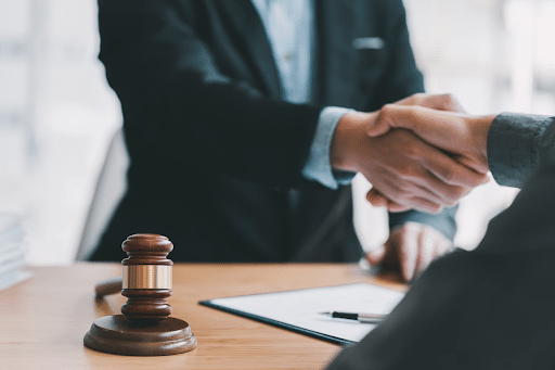 A catastrophic injury lawyer shaking their client's hand after a personal injury trial. On their desk is paperwork and a gavel.