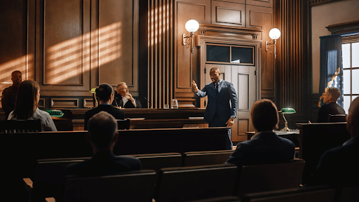 A car accident lawyer at trial in front of the judge, defending a case. There are other attendees sitting in the courtroom watching.