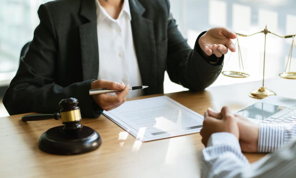 A car accident lawyer is discussing paperwork with their client. In front of them is a gavel and the scales of justice.