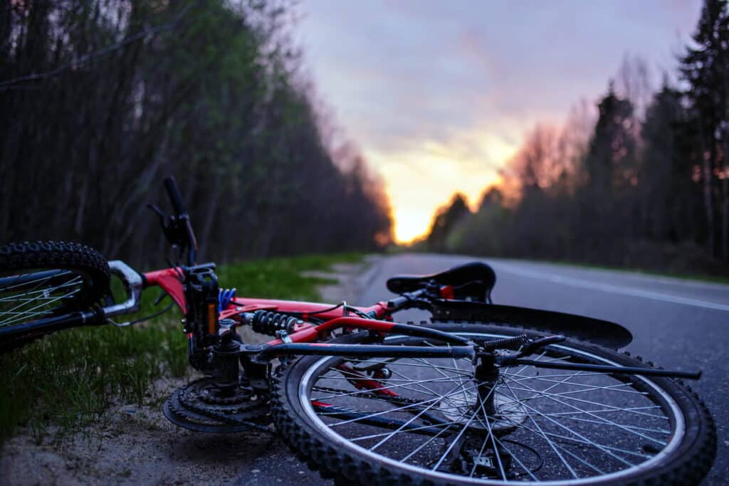 A discarded red bicycle on the side of the road after being in a bicycle accident.